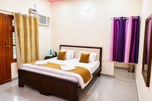 A hotel room with a bed, curtains, an air conditioning unit, a bedside table with a kettle, and a trash bin. - The Ushmaya Wellness Resort Rishikesh (Rishikesh)