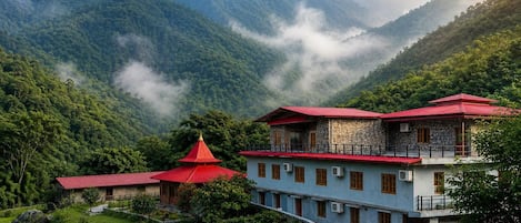 Un edificio tradicional con techo rojo, rodeado de exuberante vegetación y montañas.