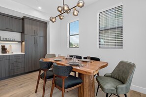 Zona pranzo moderna con tavolo in legno, quattro sedie e lampadario.
