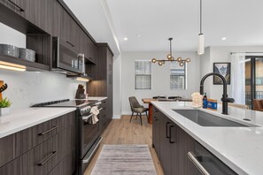 Una cocina moderna con armarios de madera oscura, encimera blanca, horno empotrado y una isla grande con lavamanos.