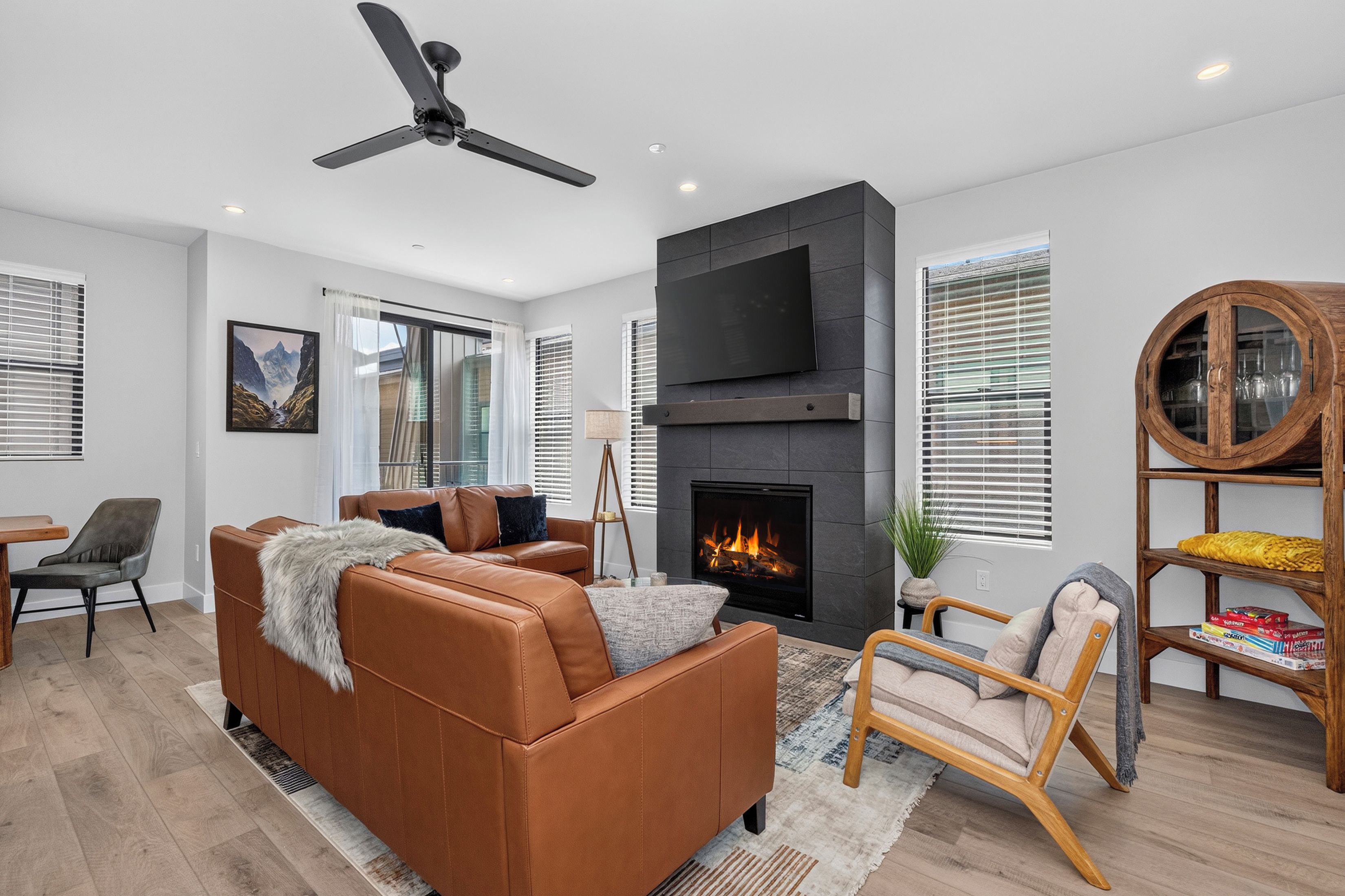 A modern living room with a fireplace, leather sofa, and a ceiling fan.
