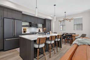 A modern kitchen with dark cabinetry, stainless steel appliances, and a central island with bar stools. - Granby Station Townhomes Unit 3B Rooftop deck, views, garage parking (Granby)