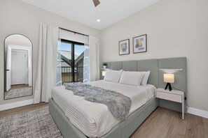 Una camera da letto con un letto, un comodino, una lampada, uno specchio e una finestra con tende.