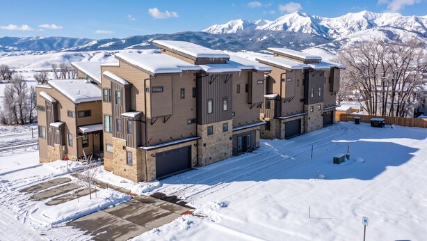 A multi-story building with a snow-covered roof and a view of snow-covered mountains in the background.