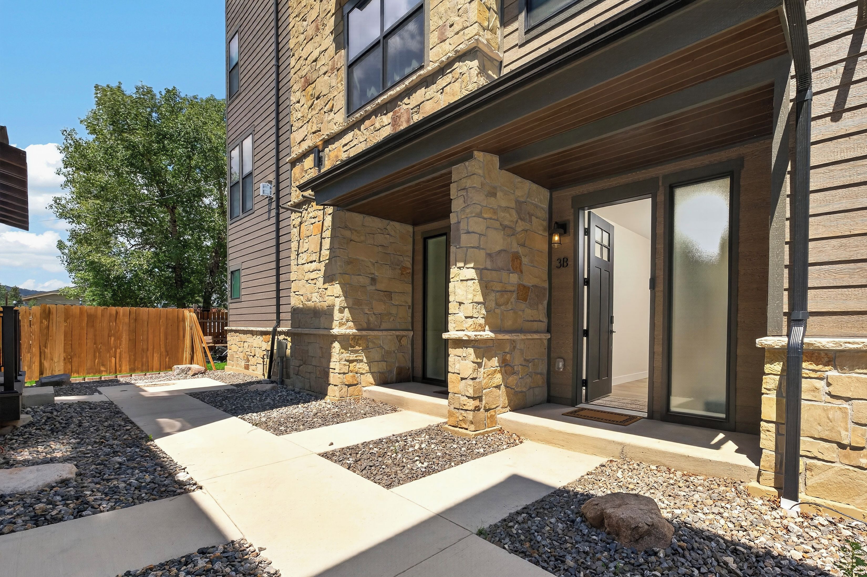 A modern building with a stone facade, a covered patio area, and a wooden fence in the background.