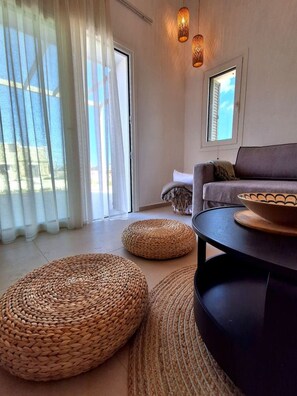 A modern living room with a sofa, a round coffee table, and woven ottomans. - Fanes Breeze Lodges - Lodge Sykia (Fanes)