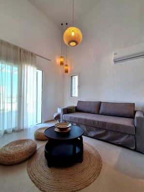 A modern living room with a sofa, a coffee table, and a hanging light fixture. - Fanes Breeze Lodges - Lodge Sykia (Fanes)