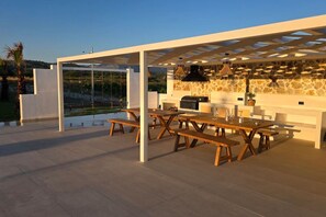 An outdoor patio with a stone wall, wooden tables, and a grill. - Fanes Breeze Lodges - Lodge Sykia (Fanes)