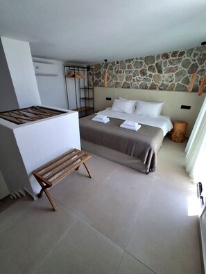 Una camera da letto con un letto, una panca, un muro in pietra e una finestra.