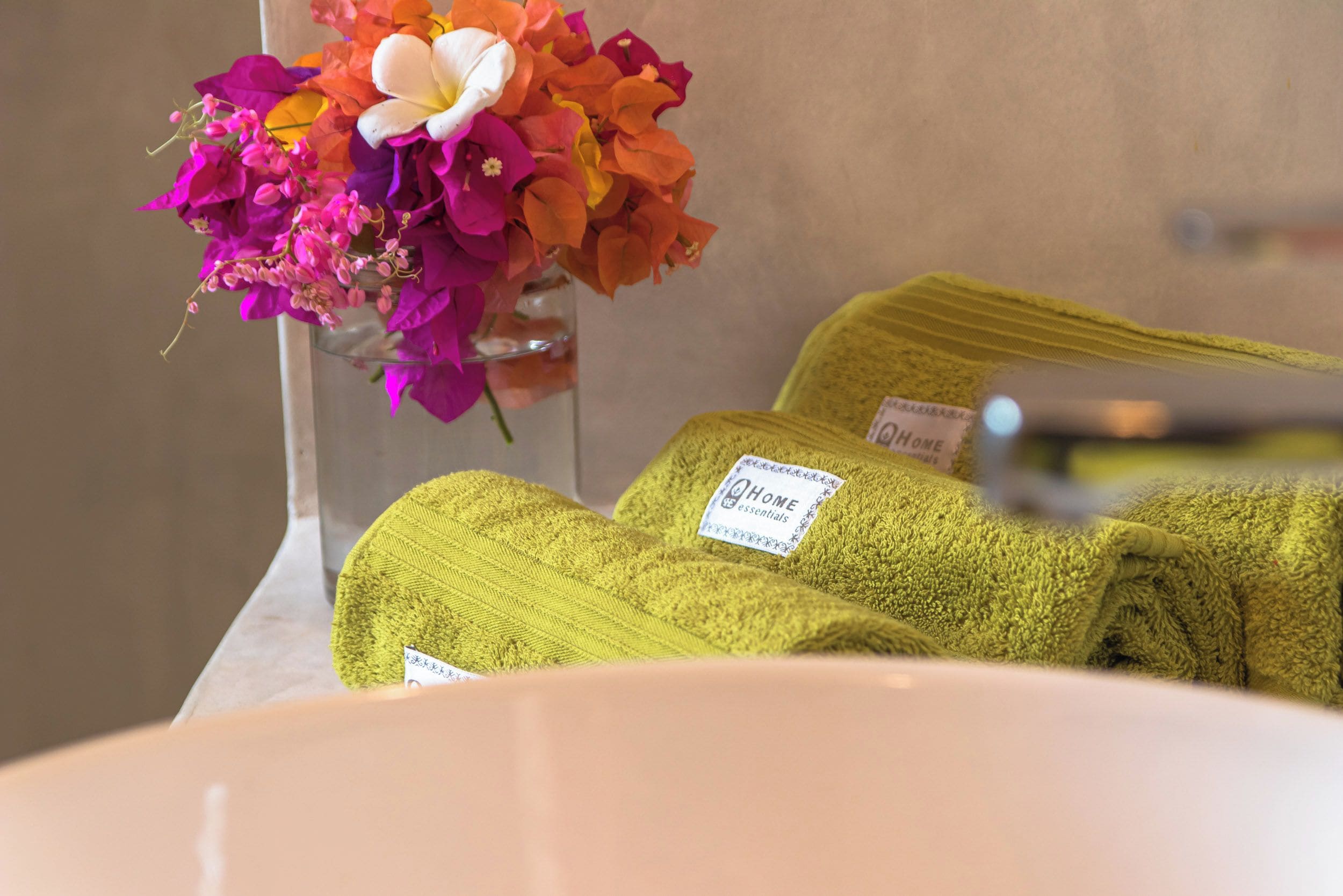 Ein Badezimmer mit einem Waschbecken, einer Glasvase mit Blumen und grünen Handtüchern.
