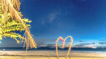A beach with a starry night sky, a palm tree, and a decorative arch made of branches and flowers.