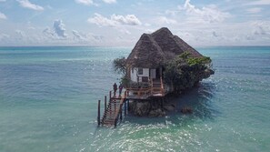 A thatched-roof bungalow with a wooden deck and a staircase leading to a small porch. - Pingwe Beach Apartments (Michamvi)
