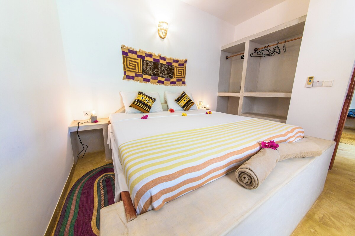 A hotel room with a bed, a bedside table, a wall-mounted light, a patterned tapestry, and a wardrobe.