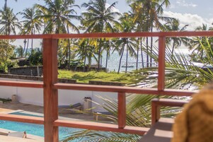A pool area with a view of palm trees and the ocean.