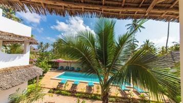 A pool area with a thatched roof, palm trees, and lounge chairs.