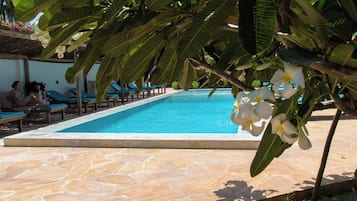 A swimming pool with lounge chairs and a covered seating area.