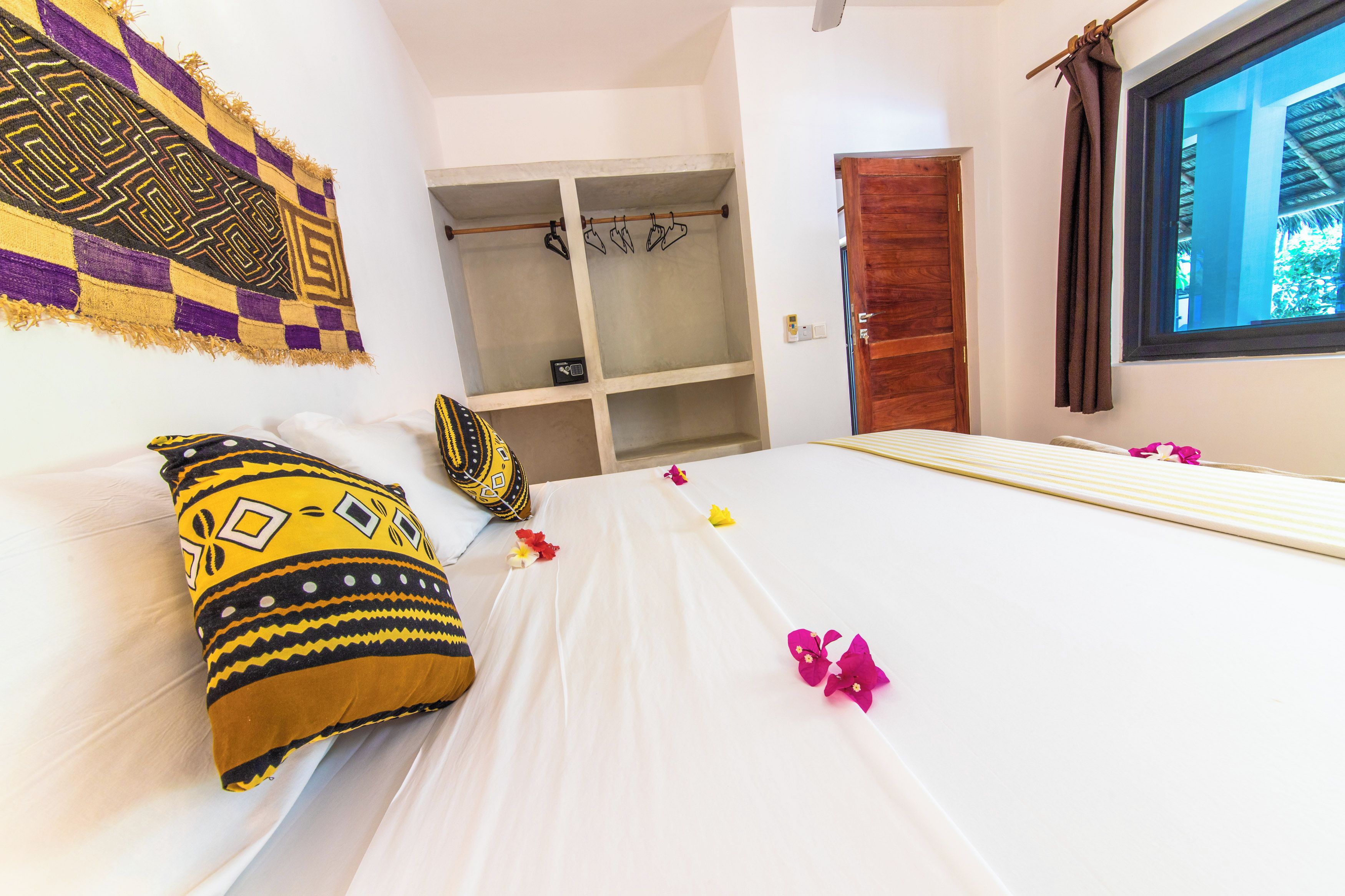A hotel room with a bed, a wardrobe, a window, and a wall with a patterned tapestry.