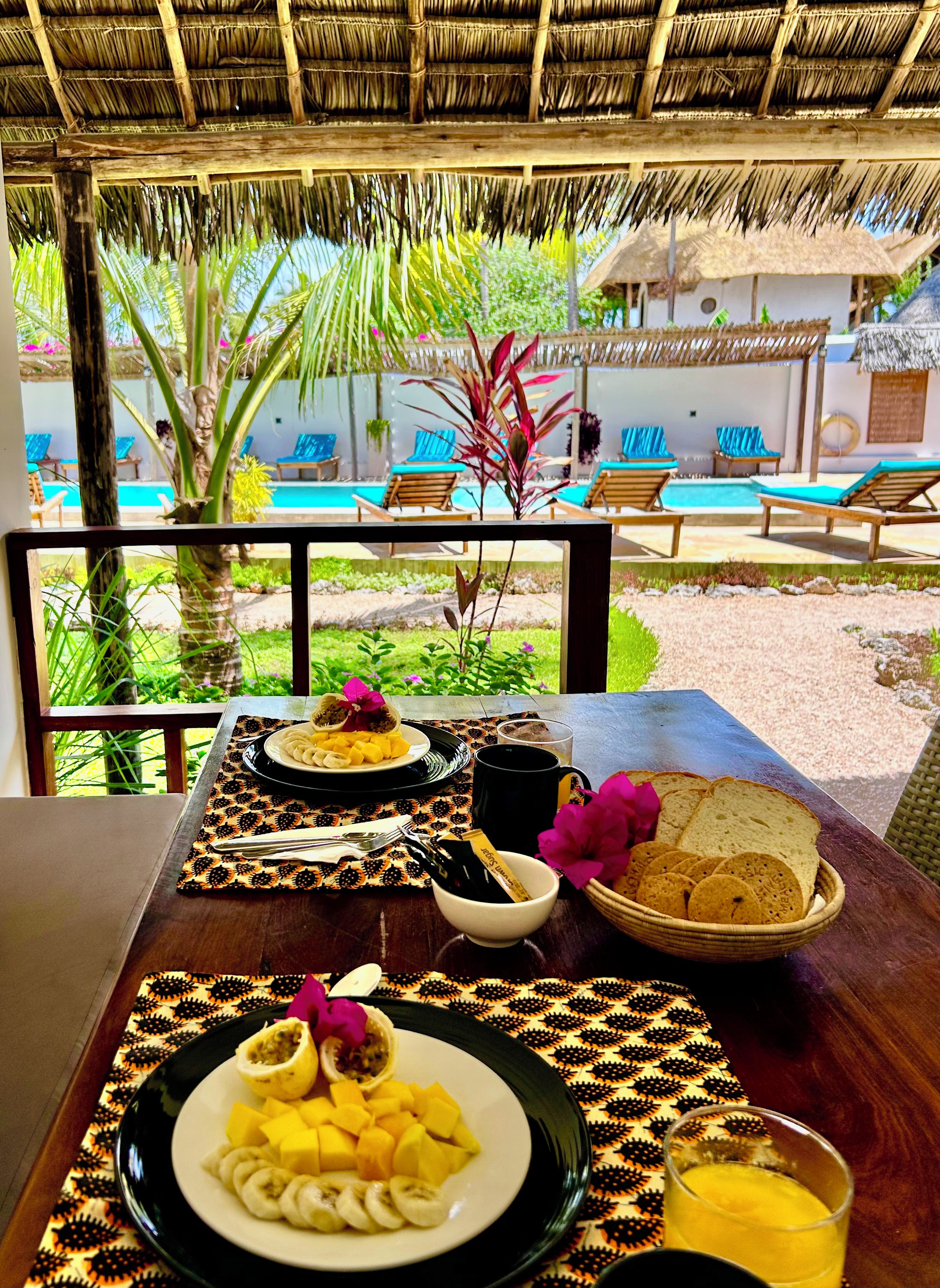 A breakfast table with plates of food, a glass of juice, and a basket of bread.