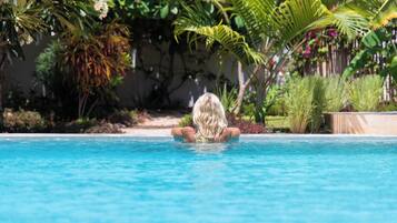 A swimming pool with clear blue water, surrounded by lush greenery and palm trees.