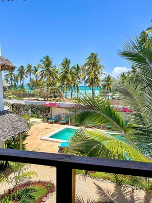 A pool area with a view of the ocean, palm trees, and a thatched-roof structure. - Pingwe Beach Apartments (Michamvi)