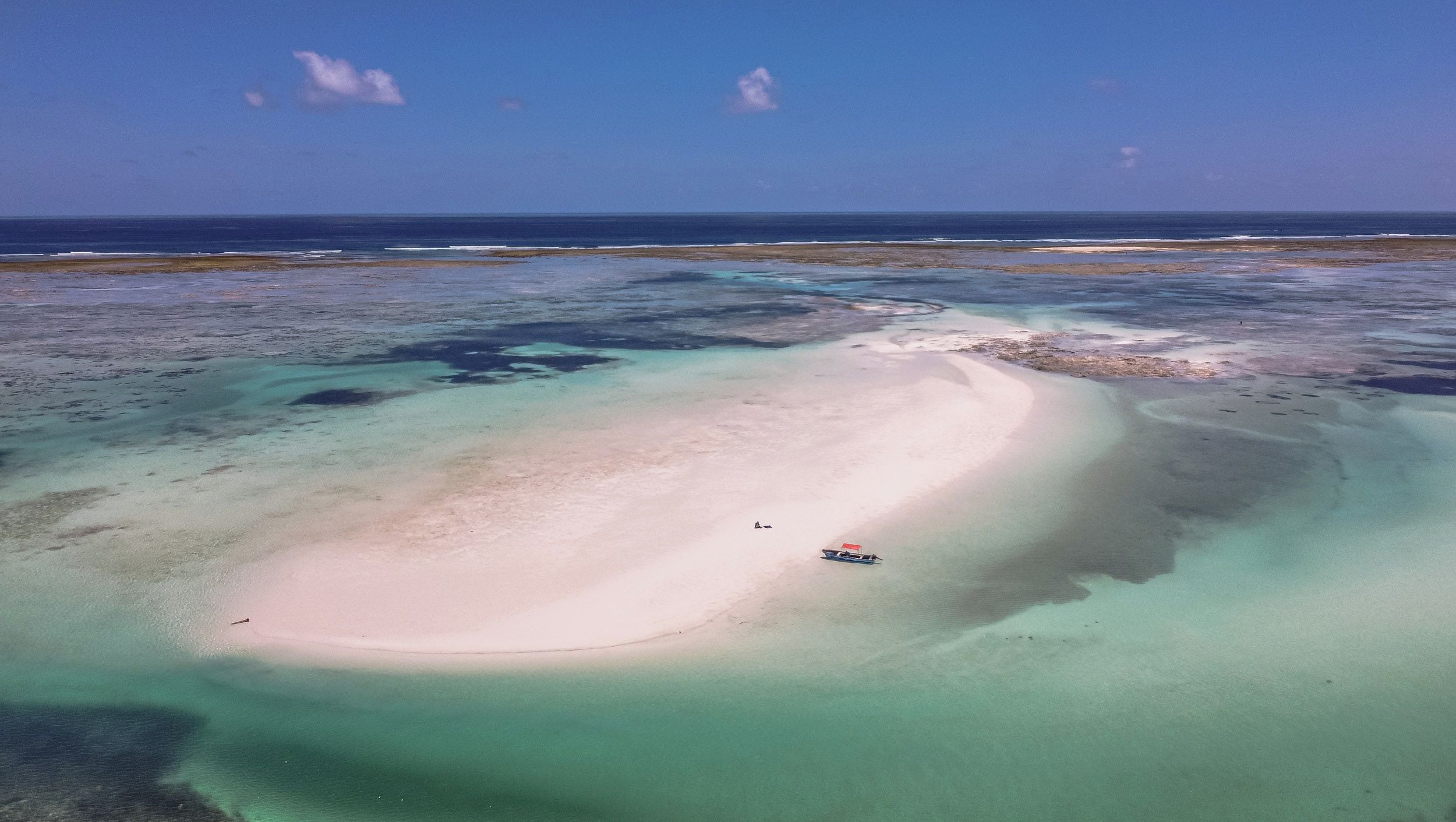 Ein Strand mit klarem türkisblauem Wasser und einem Boot, das in der Nähe der Küste vor Anker liegt.