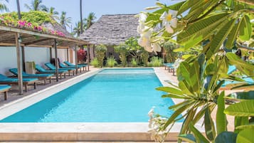 A pool area with lounge chairs and a thatched-roof structure.