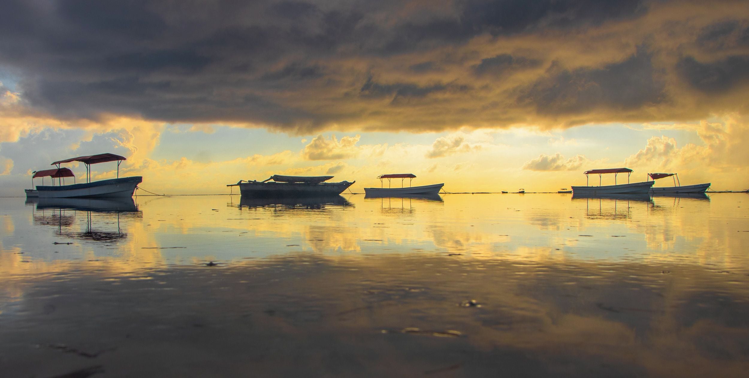 Une étendue d’eau calme où plusieurs bateaux sont amarrés, et où le ciel se reflète.