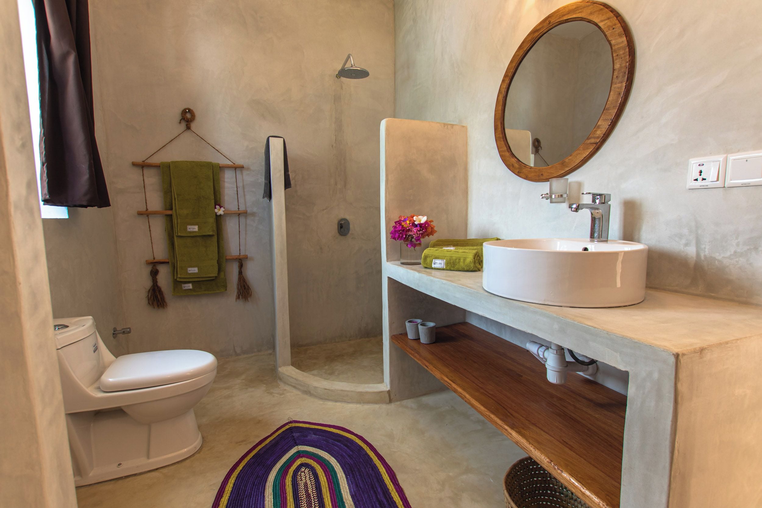 A bathroom with a toilet, a shower, a sink with a mirror, and a towel rack.