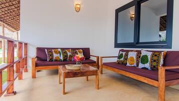 A room with two wooden sofas with patterned cushions, a wooden coffee table with a woven basket and flowers, and a large window with a dark frame.