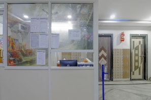 Un espace d’accueil d’hôtel avec un panneau d’affichage où sont accrochées diverses informations, un extincteur fixé au mur, et un bureau bleu équipé d’un ordinateur et d’une poubelle.