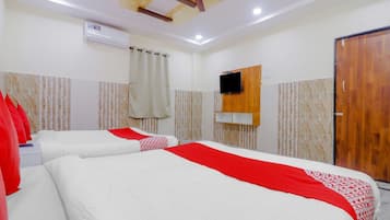 Habitación de hotel con dos camas, ventilador de techo, unidad de aire acondicionado, televisor montado en la pared y puerta de madera.