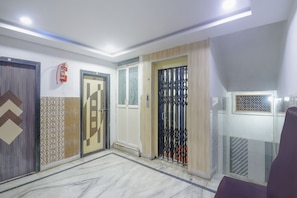 Un couloir avec trois portes, un extincteur et un sol à motifs.