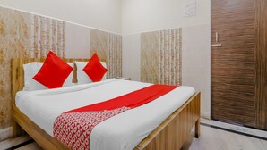 A hotel room with a bed, two red pillows, a white bedspread, and a wooden headboard. - Deluxe Hotel Ashoka Grand (Sadasivpet)