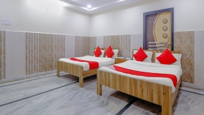 A hotel room with two wooden beds, red pillows, a ceiling fan, and a marble floor. - Deluxe Hotel Ashoka Grand (Sadasivpet)