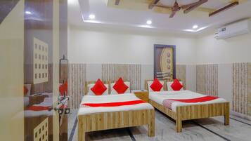 A hotel room with two wooden beds, red pillows, a ceiling fan, and an air conditioning unit.