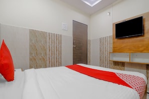 Une chambre d’hôtel avec un lit, un téléviseur fixé au mur et une tête de lit en bois.