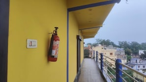 A fire extinguisher mounted on a yellow wall in a corridor with a railing and a view of buildings in the background.