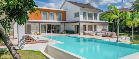 Una casa moderna de dos pisos con piscina, mobiliario exterior y un jardín bien cuidado.