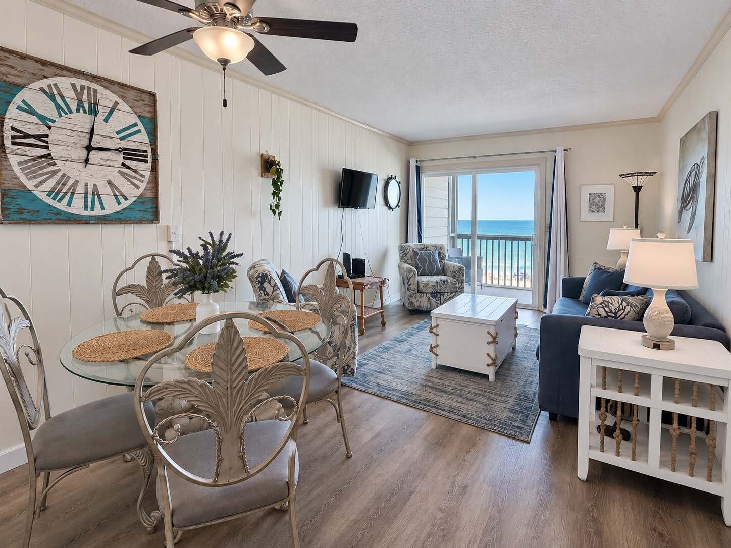 A living room with a glass dining table, chairs, a sofa, and a ceiling fan.