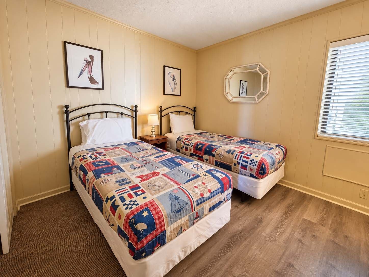 A bedroom with two beds, a wooden floor, and a window with blinds.