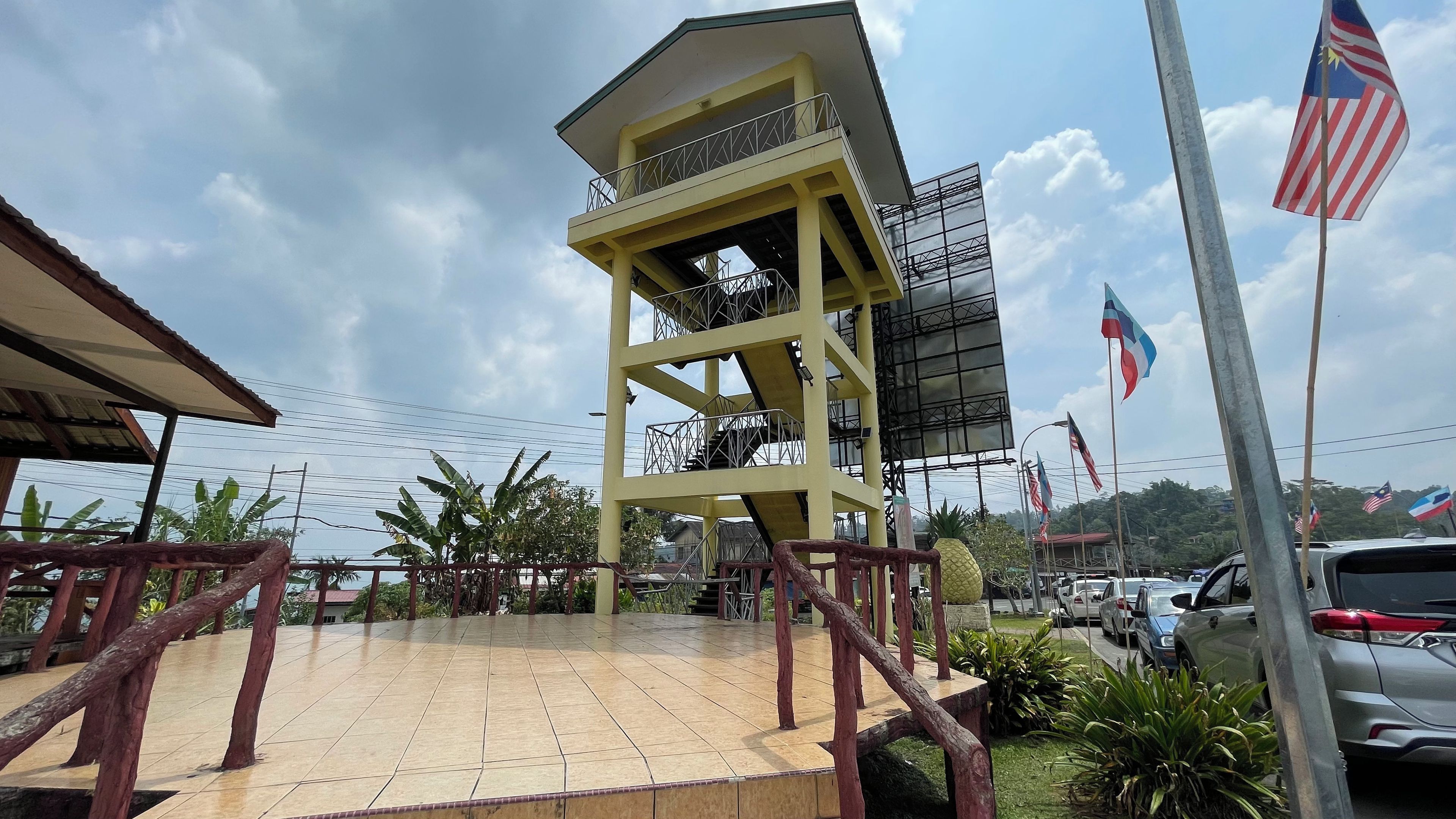 A multi-story building with a balcony, surrounded by parked cars and flags.