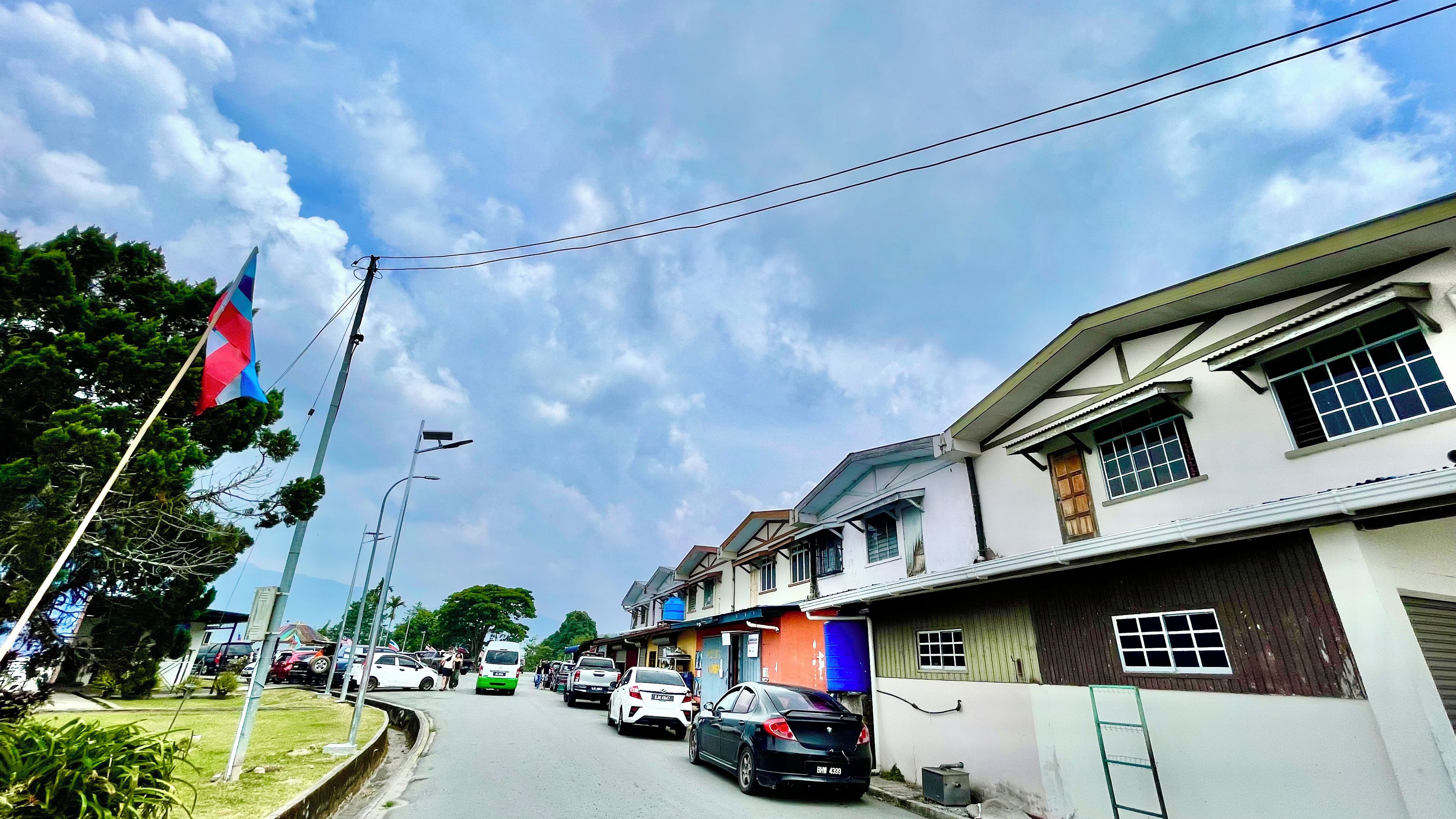 A street with residential buildings, parked cars, and a flag.