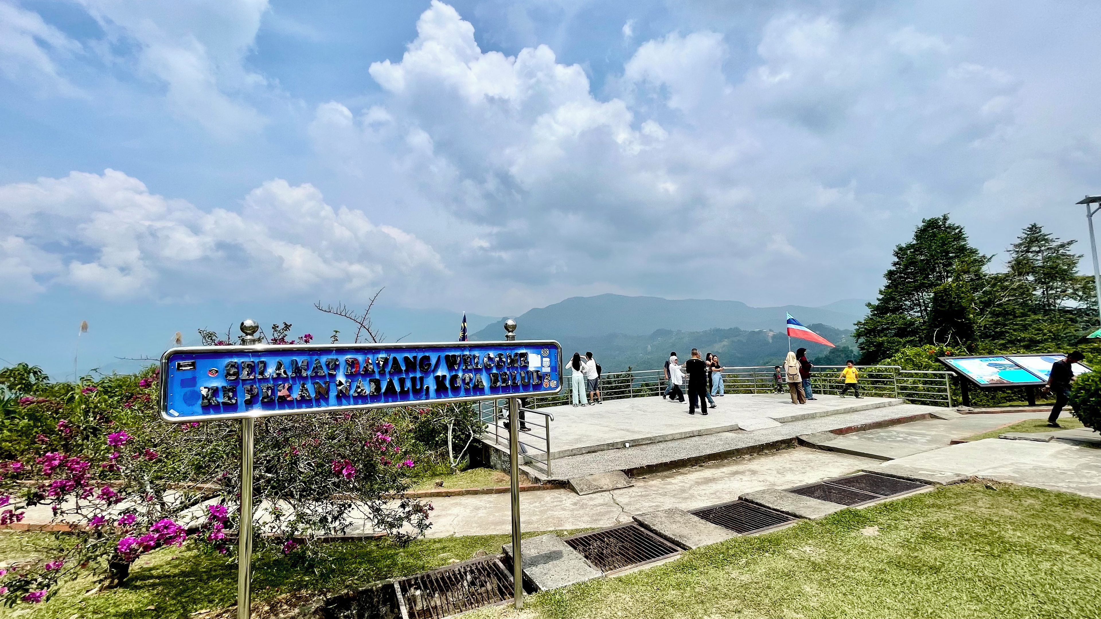 A signboard with text, a paved area with steps, and a view of mountains in the background.