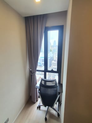 A room with a desk and chair, a window with curtains, and a view of city buildings. - Luxury Condo at Ashton Asoke 1 Min to BTS & MRT⁠ (Krung Thep Maha Nakhon)