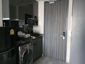 A compact kitchen with a microwave, a dish rack, a washing machine, and a grey sliding door. - Luxury Condo at Ashton Asoke 1 Min to BTS & MRT⁠ (Krung Thep Maha Nakhon)