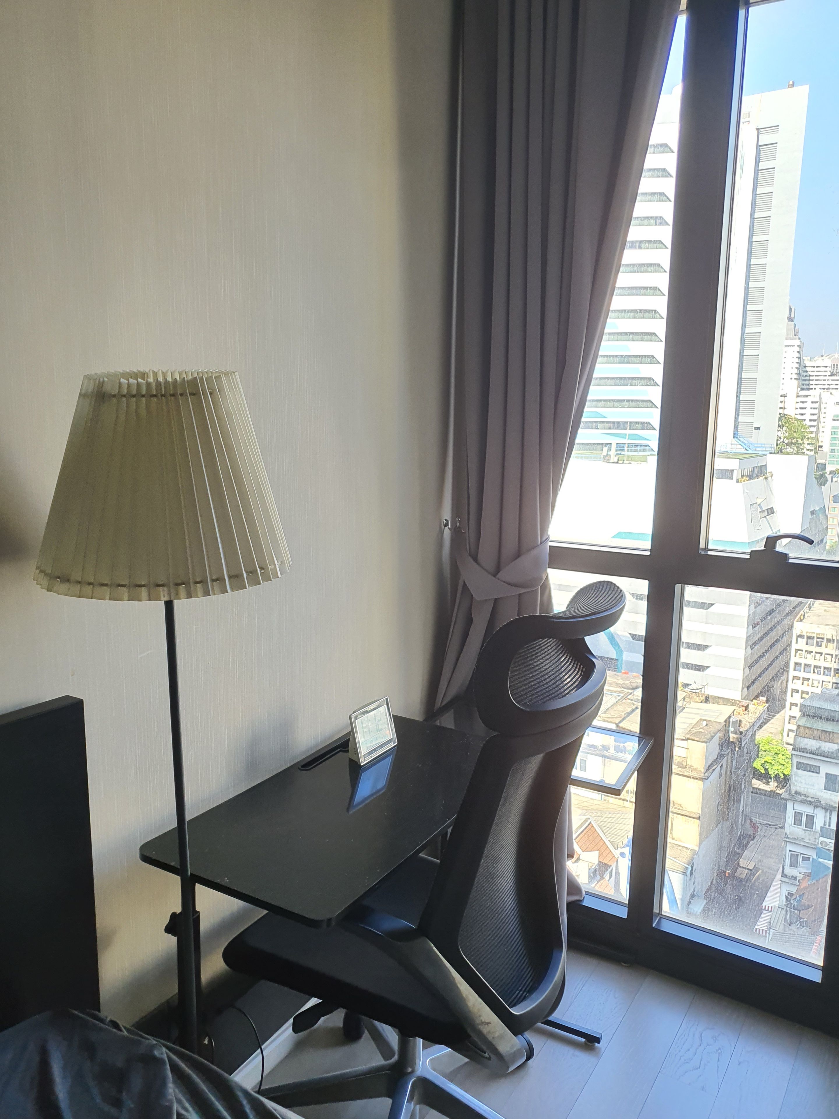 Ein Hotelzimmer mit Schreibtisch, Stuhl, Lampe und Blick auf die Stadt durch große Fenster.