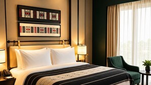 Ett hotellrum med en stor säng, sänglampor, en röd bänk, en grön stol och utsikt över omgivningarna genom ett fönster.