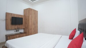 Un dormitorio con cama, un armario de madera, televisor montado en la pared y mesita de noche.