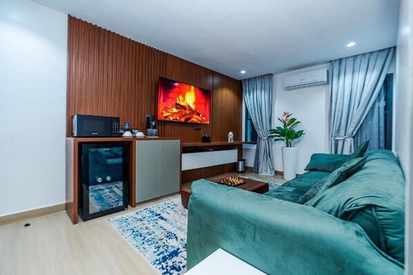 A modern living room with a green sofa, a small coffee table, a TV mounted on a wooden wall, and a fireplace.
