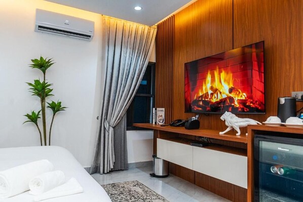 A modern hotel room with a flat-screen TV, a wooden entertainment unit, a bed with white linens, a small plant, and a wall-mounted air conditioner.